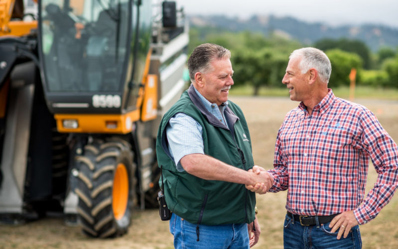 American AgCredit loan officer and farmer shaking hands in front of farm equipment