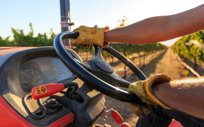 Closeup of a farmer driving tractor in vineyards, farm equipment financing